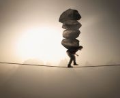 man walking tightrope carrying four boulders on his back.jpg from in man