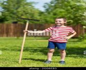 a little cheerful boy stands and holds a rake in his hand ready to work in the garden of a country house 2g08eb3.jpg from pak with small biy