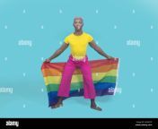 full body barefoot black gay in colorful clothes looking at camera and waving rainbow flag behind legs during lgbt pride event against turquoise backg 2k4gcye.jpg from gay man se