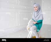 muslim teen 9 year girl in grey hijab and blue dress is playing riding on toy horse rocking chair in her white modern room t8nymp.jpg from teen9